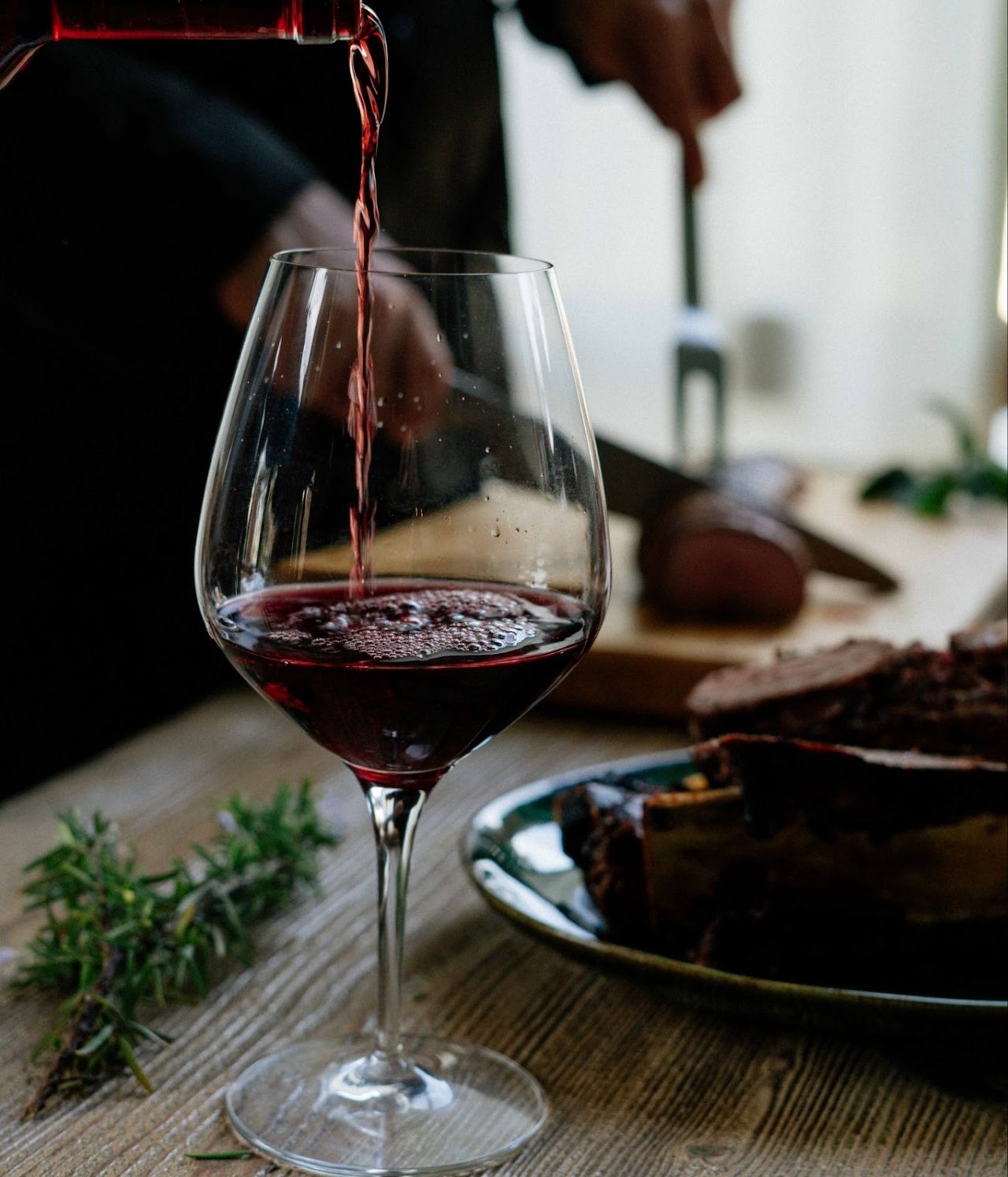 Red wine being poured into a glass beside a shared plate